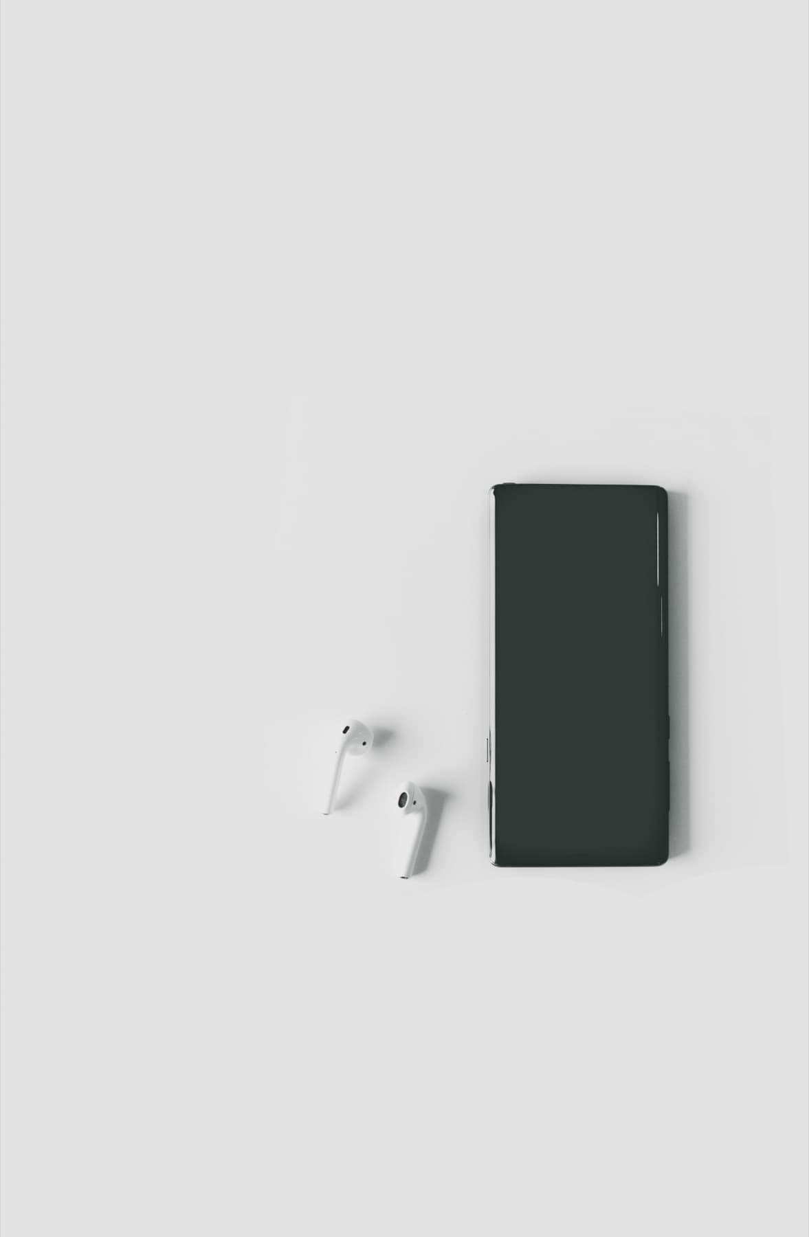 Smartphone and wireless earphones on a white surface